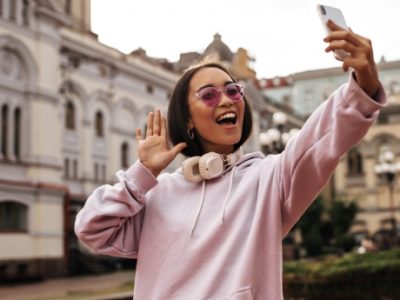 cool-teen-young-woman-pink-hoodie-stylish-sunglasses-takes-selfie-holds-phone-poses-with-headphones-outside.jpg